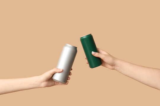 Female hands with fresh beer in cans on beige background