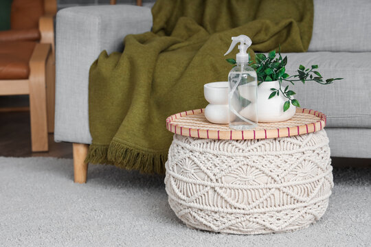 Bottle of aroma spray with plant on pouf in living room
