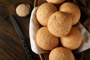 Wicker bowl of fresh buns with sesame seeds on wooden background