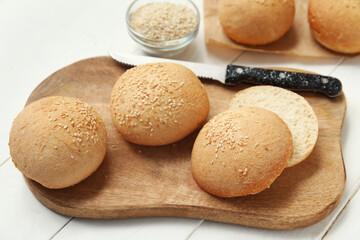 Board of fresh buns with sesame seeds on white wooden background