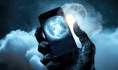 Werewolf hand holds phone showing moon amidst dark, cloudy night sky