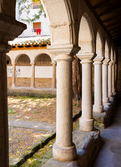 Fototapeta premium Serene shaded gallery at Sant Llorenc de Morunys with ancient stone columns and arches surrounding square sunlit monastery courtyard on summer day, Catalonia, Spain
