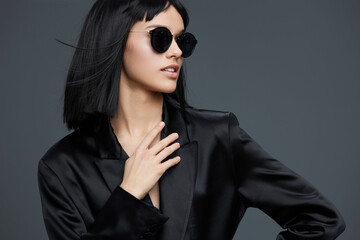 Asian woman in black suit and sunglasses striking a confident pose with one hand on her hip and the...