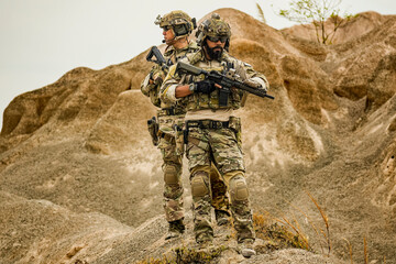 A group of military men in combat gear patrol in the middle of a desert and tropical jungle....