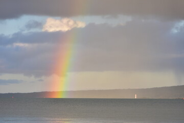 Almost vertical bright rainbow next to lighthouse with Rangitoto Island in background. Location: Takapuna Auckland New Zealand