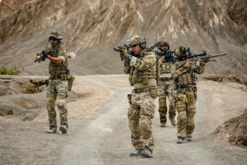 Fototapeta premium A group of military men in combat gear patrol in the middle of a desert and tropical jungle. Soldiers in full combat gear in dry weather conditions assemble and march on a mission.