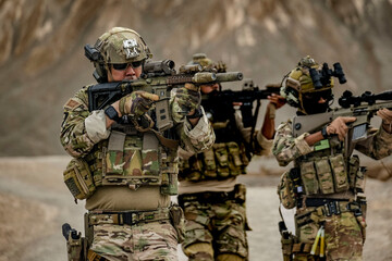 A group of military men in combat gear patrol in the middle of a desert and tropical jungle....