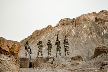 A group of military men in combat gear patrol in the middle of a desert and tropical jungle....