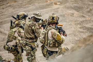 Fototapeta premium A group of military men in combat gear patrol in the middle of a desert and tropical jungle. Soldiers in full combat gear in dry weather conditions assemble and march on a mission.