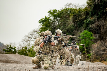 Fototapeta premium A group of military men in combat gear patrol in the middle of a desert and tropical jungle. Soldiers in full combat gear in dry weather conditions assemble and march on a mission.
