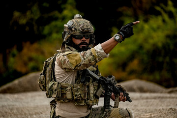 A group of military men in combat gear patrol in the middle of a desert and tropical jungle. Soldiers in full combat gear in dry weather conditions assemble and march on a mission.