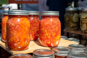 Multiple glass jars filled with fresh ingredients for homemade salsa. The containers have peppers,...