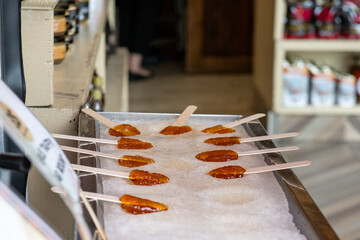 A traditional Canadian sweet candy made of boiled maple sap laid on a tray of clean snow. The rolls of thick syrup have made round lollipops using a small wooden stick. The pops are street food.