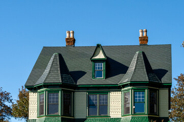 The exterior attic of an old cottage. The exterior wooden wall is a yellow clapboard with green trim. There are two bay windows and a dormer on the front top floor of the residence.  © Dolores  Harvey
