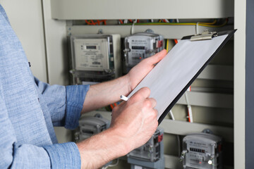 Technician worker with clipboard inspecting electricity meter, closeup