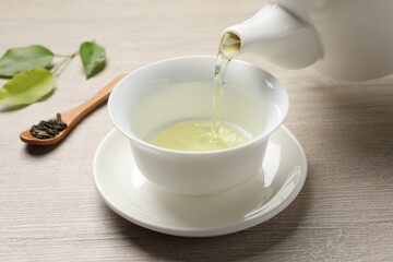Pouring refreshing green tea into cup at wooden table, closeup
