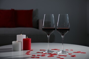 Burning candles, wine in glasses and paper hearts on table indoors