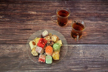 A plate with a variety of oriental sweets and two cups of hot black tea on a wooden table.