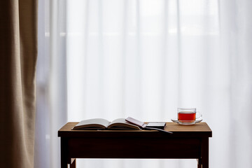 窓際の机に置かれた紅茶とノートと携帯電話