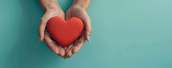 Obraz premium Hands holding a red heart symbolizing love and care. Light turquoise background giving a calm and peaceful feel.
