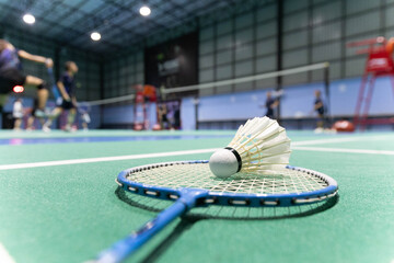 The shuttlecock sits on a bilton racket on the green badminton court. Background taken in low light