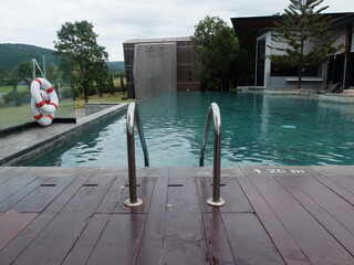 symmetry shape of outdoor swimming pool ladder in front of the blue water in the hotel with the mountain in the background.