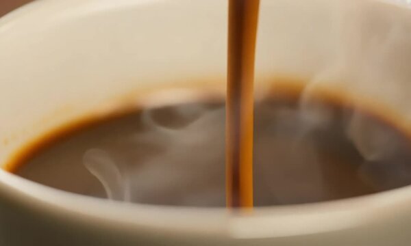 A cup of coffee is poured into a white cup. The coffee is brown and has a rich aroma