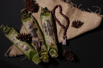 Grilled rice wrapped in banana leaf, served on brown burlap fabric with a black background, evoking a rustic, traditional vibe.