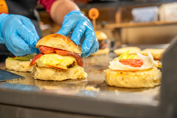Cook assembling delicious burger wearing blue gloves in kitchen