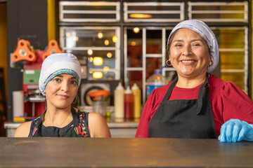 Two happy cooks smiling behind counter in a fast food restaurant kitchen