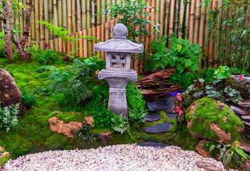 Minimal Japanese garden in home with small stone lantern and bamboo fountain and moss and flowers.
