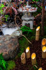 Minimal Japanese garden in home with small stone lantern and bamboo fountain and moss and flowers.
