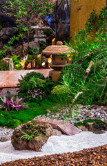 Minimal Japanese garden in home with small stone lantern and bamboo fountain and moss and flowers.
