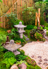 Minimal Japanese garden in home with small stone lantern and bamboo fountain and moss and flowers.
