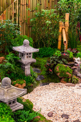 Minimal Japanese garden in home with small stone lantern and bamboo fountain and moss and flowers.
