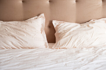 Messy bed with crumpled pillows and sheets on beige headboard.