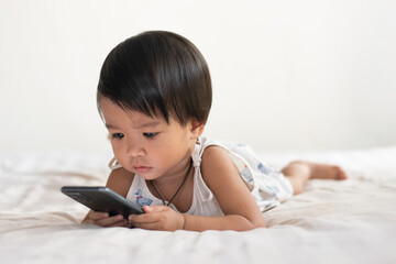 Children, lovely Asian women, are lying on the mattress at home watching their mobile phones.