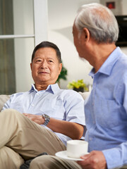 Obraz premium two happy senior asian men sitting and chatting on couch at home
