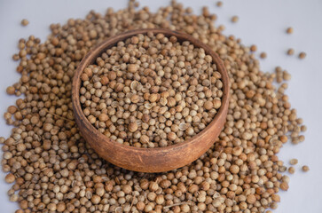 Coriander seeds in a wooden plate on a white background