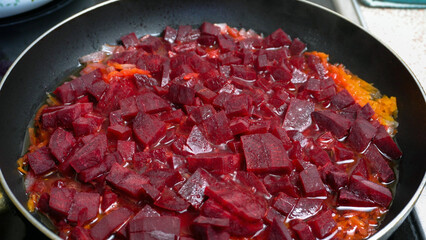 Chopped beets, carrots, and onions are sauteed in oil in a frying pan