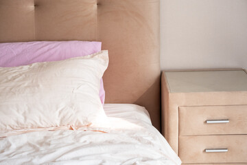 Unmade bed with pillows against beige headboard featuring soft lighting.