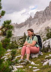  Female traveler in her 50s enjoys a trip in mountains. Magnificent views.Woman sitting on a rock. Healthy lifestyle, hiking