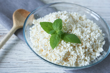 Bowl with tasty cottage cheese and mint on table, closeup