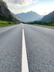Asphalt road in the mountains under the blue sky with clouds.