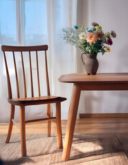 A wooden table with a vase of flowers sitting on top of it next to a wooden chair