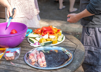 Woman and man chopping vegetables zucchini, eggplant and sweet pepper, sausages preparing to grill.