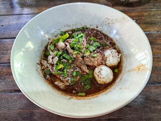 Noodles with pork, vegetables, meatballs, and soup in a bowl.