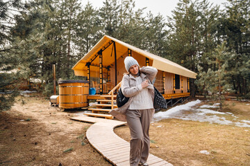 A woman in a winter jacket walks along a wooden path in glamping.