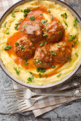 Corn polenta with cream and cheese served with meatballs in spicy gravy close-up in a bowl on the table. Vertical top view from above