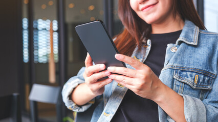 Closeup image of a young woman holding and using mobile phone in cafe